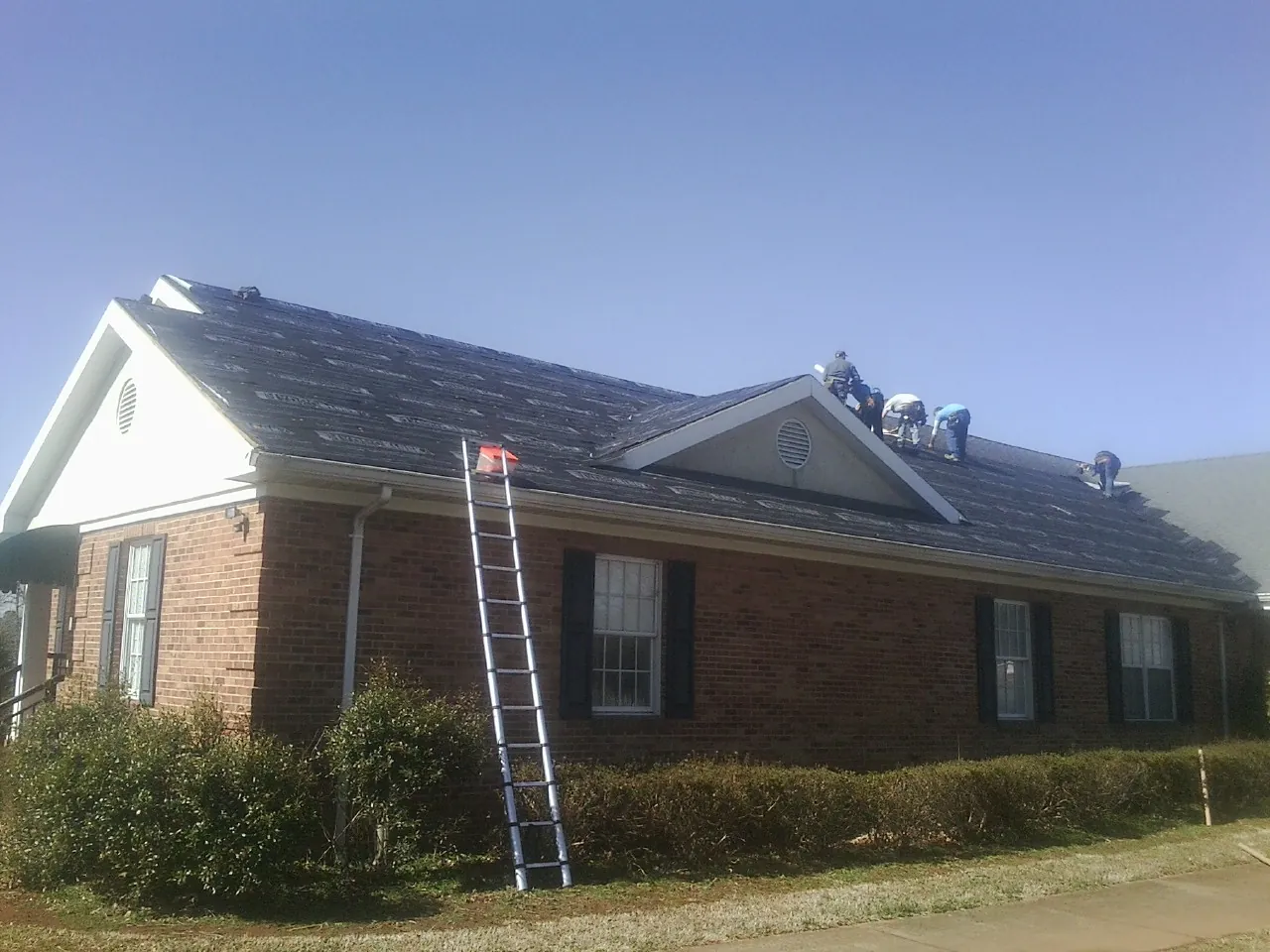 Crew tearing shingles off a brick ranch roof with a ladder set — Emergency Roof Repair work by our crew in West Suffield