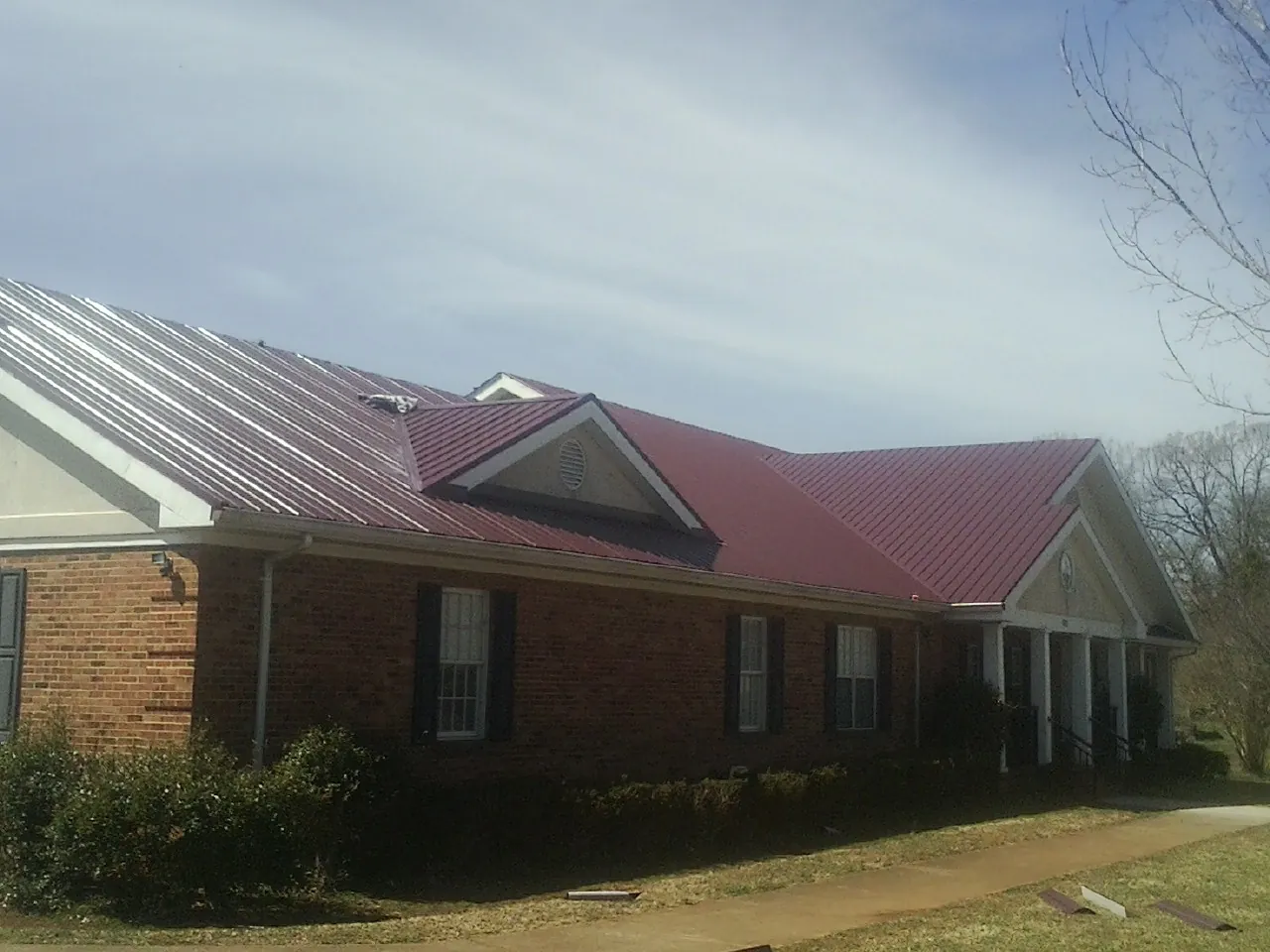 Red metal roof with gabled entries on a long brick building, from a Hail Damage Roof Repair job in West Suffield