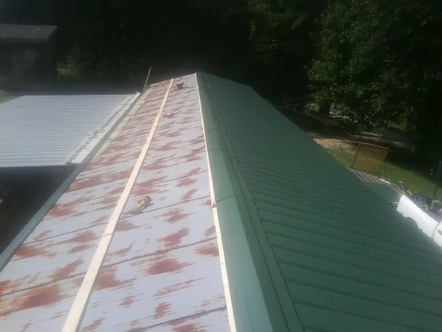 Old rusted panels beside newly installed green metal roofing — Wind Damage Roof Repair by Roofing Brothers in West Suffield