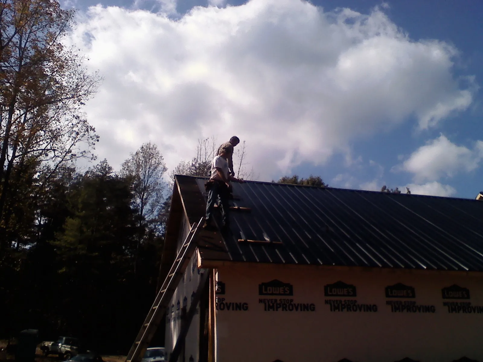 Roofer fastening dark metal panels high against a cloudy sky, from a Roof Inspection job in West Suffield