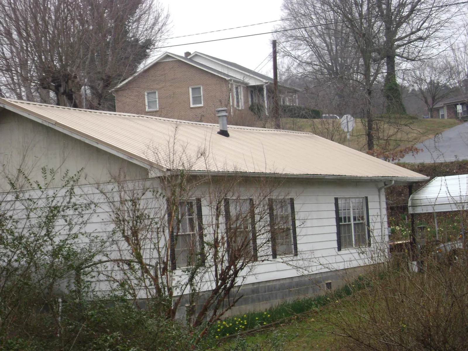 Tan metal roof on a white sided house set into a hillside — Commercial Roofing by Roofing Brothers in West Suffield